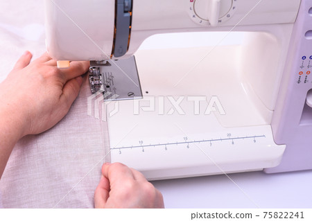 Female hands stitching light fabric on sewing machine at home.  75822241