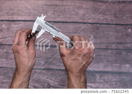 The worker measures the diameter of the drill with a caliper. The worker measures the diameter of the drill with a caliper. 75822245