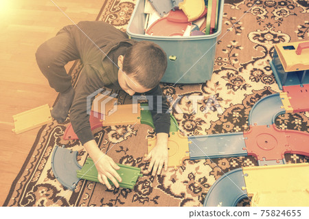charming boy plays on the floor with car track. Child playing with toys indoor. Activities for kids at home. toddler activities. Kindergarten boy at home during quarantine. toned charming boy plays on the floor with car track. Child playing with toys indoor. Activities for kids at home. toddler activities. Kindergarten boy at home during quarantine. toned 75824655