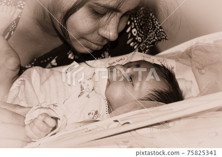 Cute newborn baby boy looks at his mother in her mother lap playing on bed. Close up. One month old Sweet little infant toddler. Indian ethnicity. Front view. Happy mothers day background image. Cute newborn baby boy looks at his mother in her mother lap playing on bed. Close up. One month old Sweet little infant toddler. Indian ethnicity. Front view. Happy mothers day background image. 75825341