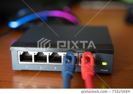 Close-up shot of a router - a red cable is connected next to the blue Ethernet cable. Concept of cabling, internet network, working with internet network. Operation and maintenance Close-up shot of a router - a red cable is connected next to the blue Ethernet cable. Concept of cabling, internet network, working with internet network. Operation and maintenance 75825684