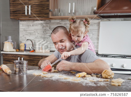a happy dad and his little daughter cook cookies together in the kitchen. joint cooking, family values 75826587