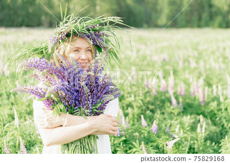 A hippy girl holding bouquet of wildflowers in her hands. Girl hid her face behind bouquet of lupins A hippy girl holding bouquet of wildflowers in her hands. Girl hid her face behind bouquet of lupins 75829168