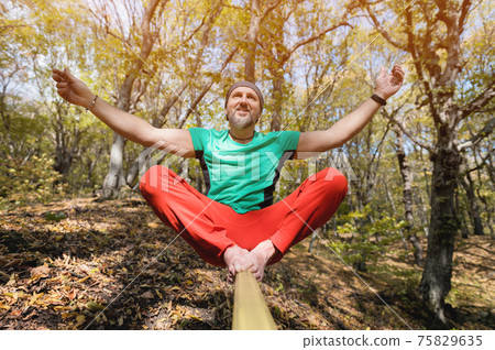 Portrait of a mature male highliner doing slackline balance training in the forest in autumn Portrait of a mature male highliner doing slackline balance training in the forest in autumn 75829635