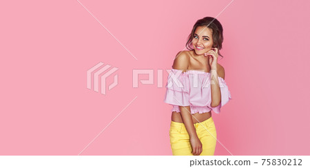 Attractive woman in yellow dress posing on pink background in studio. Looking at camera 75830212