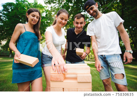 Friends playing board game outdoors in the park. Friends playing board game outdoors in the park. 75830635