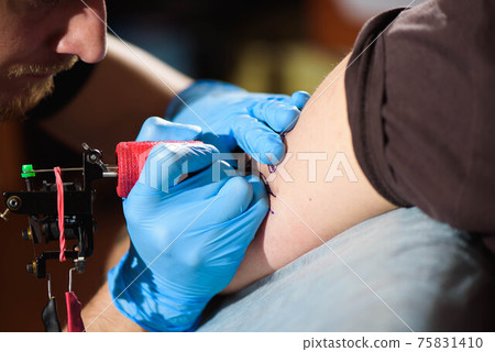 Tattoo artist creating a tattoo on a man's arm. 75831410