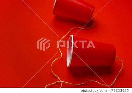 Red plastic cups connected with a thread on red background 75833935