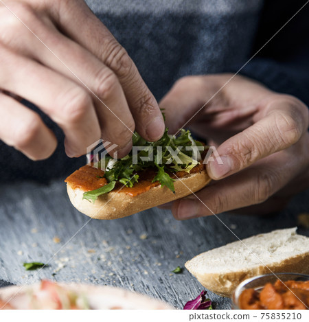 young man tops a vegan appetizer with lettuce 75835210