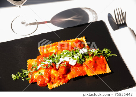 Four cheese filled ravioli in a tomato and basil sauce on the black stone plate Four cheese filled ravioli in a tomato and basil sauce on the black stone plate 75835442