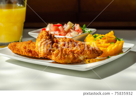 Breaded and herbed chicken breast fillet served with mashed carrots with potatoes  and  tomato salad with onions 75835932