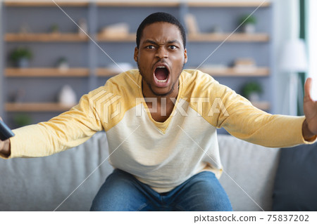 Furious black guy watching football game on TV 75837202