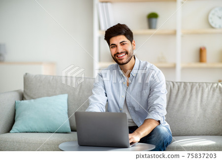 Successful remote freelancer working distantly at laptop computer and smiling to camera, sitting on couch 75837203