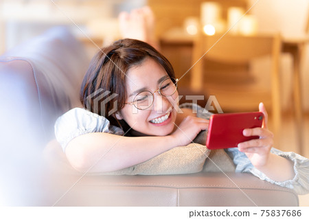 A young woman looking at her smartphone on the sofa in her living room 75837686