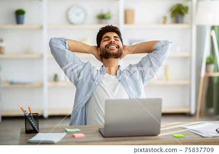 Break in work. Relaxed arab man leaning back in chair, resting after work with laptop and holding hands behind head Break in work. Relaxed arab man leaning back in chair, resting after work with laptop and holding hands behind head 75837709