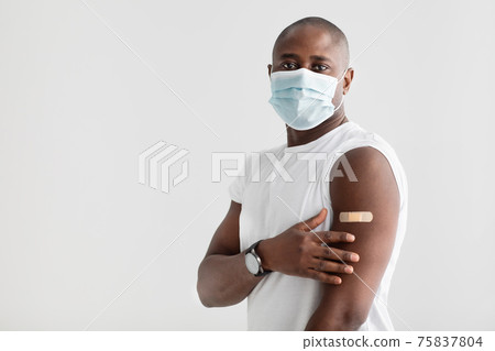 Vaccination against covid-19. Black man wearing protective mask, showing plaster on shoulder after injection, free space 75837804