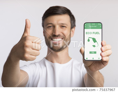 Happy guy holding smartphone with mobile app to purchase ECO fuel online, showing thumb up gesture on grey background 75837967