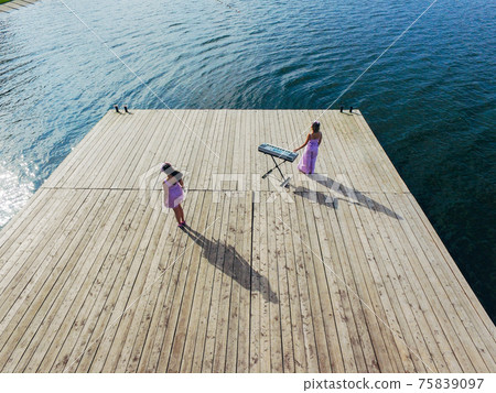 Aerial view. Two girls are standing with yonika on the pier. Surrealism Aerial view. Two girls are standing with yonika on the pier. Surrealism 75839097