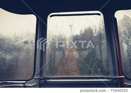 Raindrops on glass window of cableway. Sad view from overhead cable Car 75840505