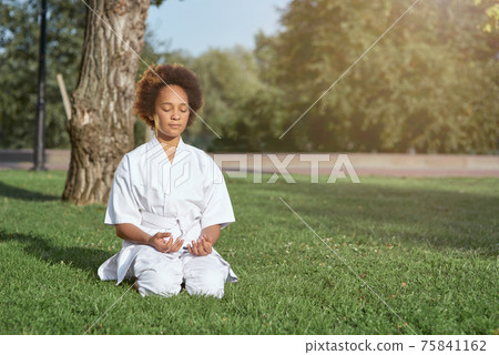 Adorable little girl in karate kimono meditating outdoors Adorable little girl in karate kimono meditating outdoors 75841162