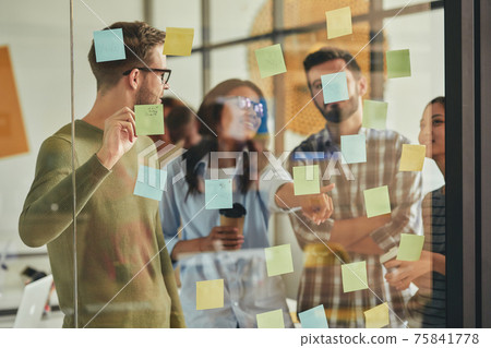 Smart and talented young people putting sticky notes on wall 75841778