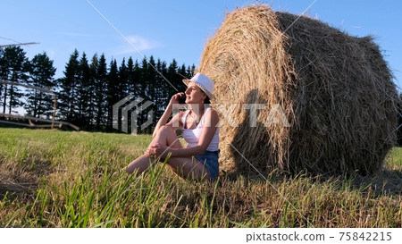 young female talking on a smartphone near a haystack. Rural area. freedom concept young female talking on a smartphone near a haystack. Rural area. freedom concept 75842215