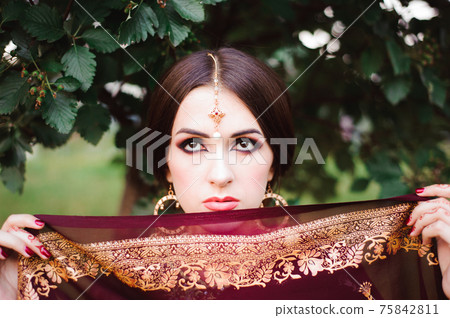 Portrait of beauty Indian model with bright make-up who hiding her face behind the veil. Hindu woman 75842811