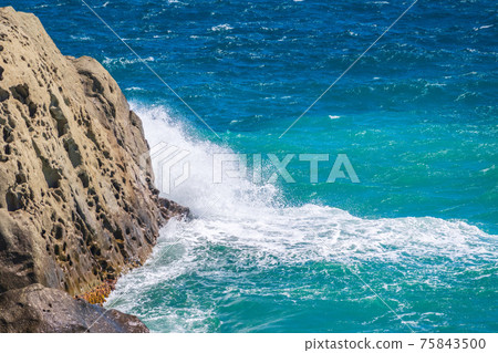 Sea waves of dark water beat against the coastal rocks. An infinite number of splashes, drops of water and white foam are scattered. Sea waves of dark water beat against the coastal rocks. An infinite number of splashes, drops of water and white foam are scattered. 75843500