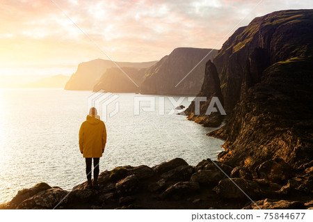 Tourist in yellow jacket looks at cliffs near Sorvagsvatn lake 75844677