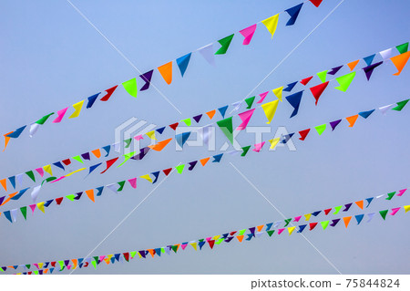triangular holiday multi colored flags are suspended on a tight string outdoors park against the background of the sky, nobody. 75844824