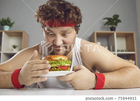 Funny chubby guy in sportswear is being tempted by unhealthy but delicious burger 75844931