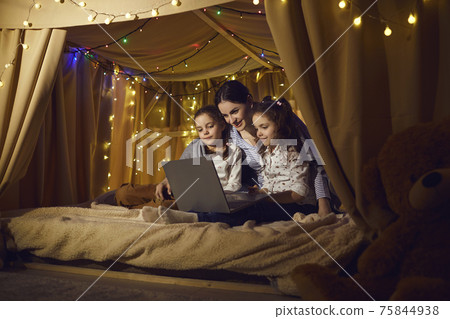 Mother with preschool daughters watching movie on laptop in kids tent at home 75844938