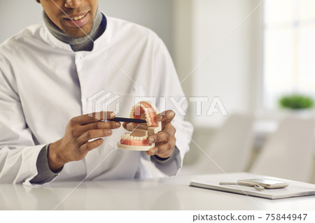 Black man doctor dentist sitting in clinic office and showing healthy gums and teeth to customer Black man doctor dentist sitting in clinic office and showing healthy gums and teeth to customer 75844947