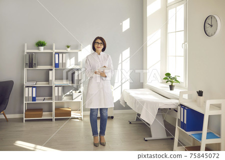 Friendly woman working as a doctor stands in her office and looks at the camera smiling. Friendly woman working as a doctor stands in her office and looks at the camera smiling. 75845072