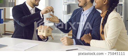 Realtor giving key from new house to interracial couple in office cropped shot 75845111