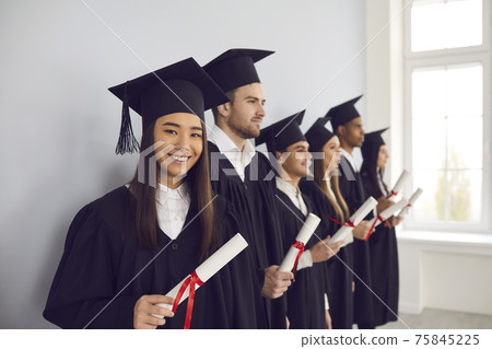 Smiling asian girl student university graduate and classmates standing with diplomas in hands Smiling asian girl student university graduate and classmates standing with diplomas in hands 75845225