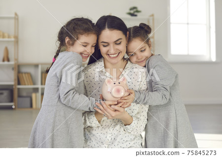 Happy single mother and her two cute little daughters holding piggy bank together 75845273