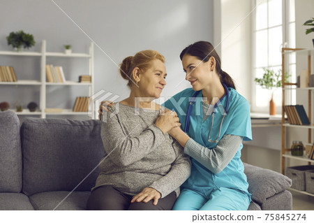 Happy doctor and senior patient sitting on couch, holding hands and looking at each other Happy doctor and senior patient sitting on couch, holding hands and looking at each other 75845274