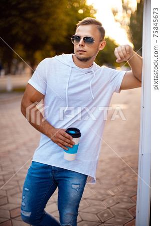 Young handsome man near city mall with cup of coffee and smartphone. Waiting for friend Young handsome man near city mall with cup of coffee and smartphone. Waiting for friend 75845673