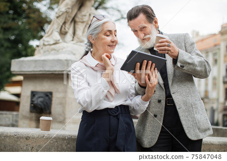 Senior man and woman with tablet drinking coffee on street Senior man and woman with tablet drinking coffee on street 75847048
