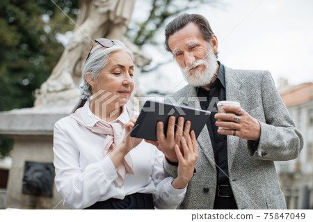 Senior man and woman with tablet drinking coffee on street Senior man and woman with tablet drinking coffee on street 75847049