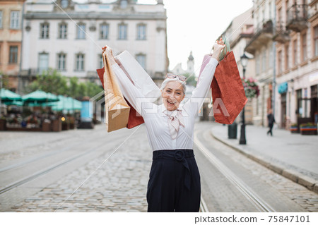 Mature lady holding shopping bags above her head Mature lady holding shopping bags above her head 75847101