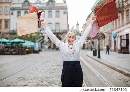 Mature lady holding shopping bags above her head 75847103