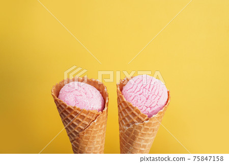 Delicious pink ice cream in a cone on a yellow background. 75847158