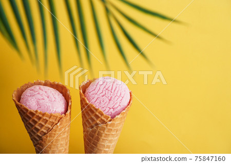 Two strawberry ice creams in a cone on a yellow background. Tropical leaf 75847160