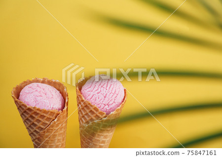 Two strawberry ice creams in a cone on a yellow background. Tropical leaf 75847161