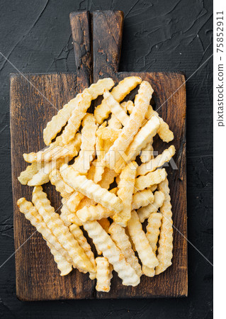 Frozen French fries potatoes, on wooden cutting board, on black background, top view flat lay 75852911