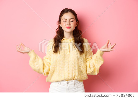 She is relaxed. Smiling young peaceful girl meditating, holding hands in zen gesture, close eyes, feel relieved and calm, standing against pink background She is relaxed. Smiling young peaceful girl meditating, holding hands in zen gesture, close eyes, feel relieved and calm, standing against pink background 75854805