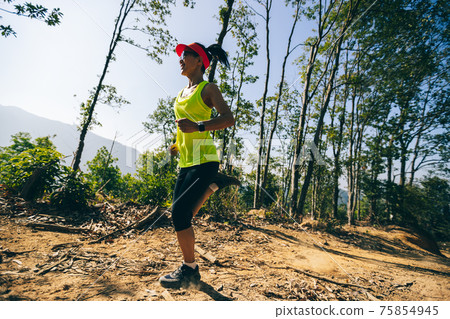 Young woman trail runner running on sunrise tropical forest mountain peak 75854945