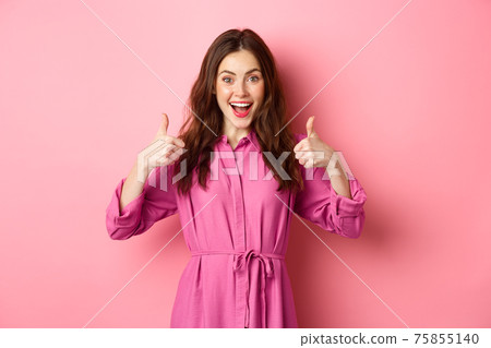 Excited girl showing thumbs up and smiling amazed, praise awesome product, standing against pink background Excited girl showing thumbs up and smiling amazed, praise awesome product, standing against pink background 75855140